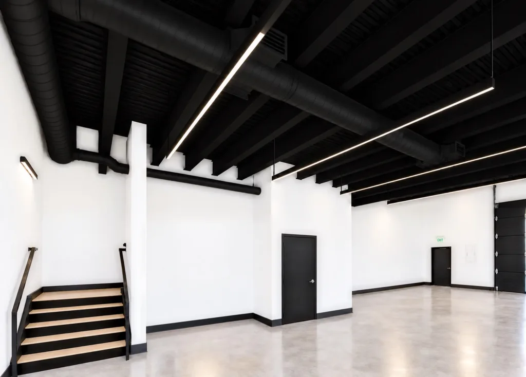 Ground-floor corner with a wood-tread stair and black railing, interior doors and an overhead door at right