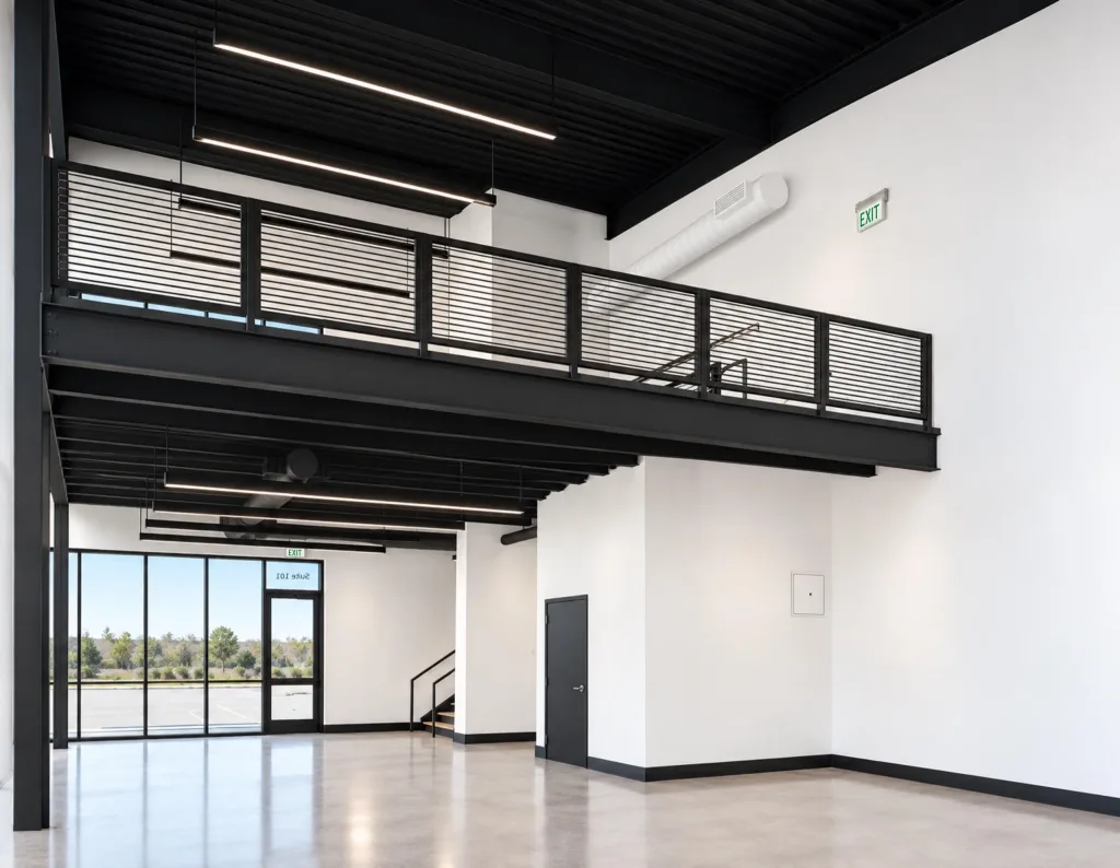 Storefront glass and an entry door beneath a black steel mezzanine with horizontal railings