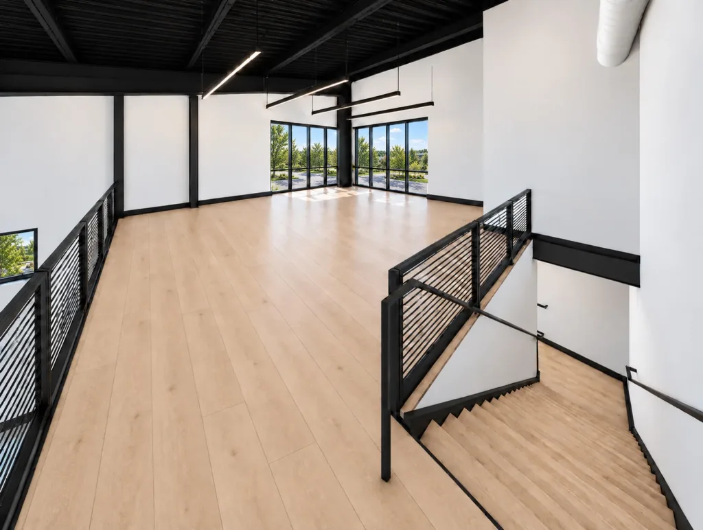 Second floor with wood-tone flooring, a black railing along the stair opening and windows at the far end