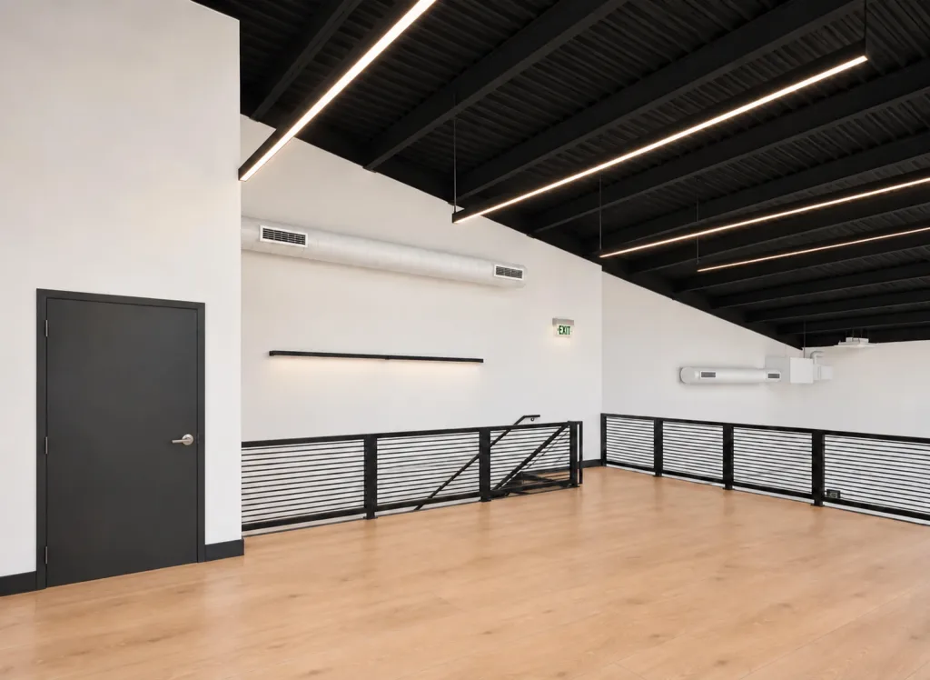 Second floor with a black door, wood-tone flooring and a railing overlooking the ground floor
